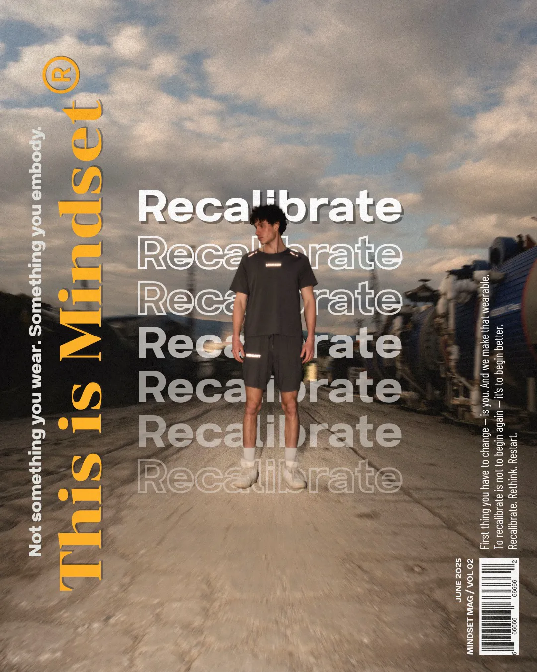 Model wearing the Mindset 'Recalibrate' technical t-shirt and shorts set in charcoal with reflective details, standing in an industrial train track setting.
